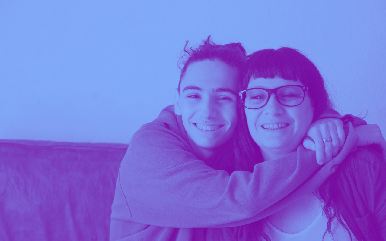 Two older people hugging and smiling towards camera.