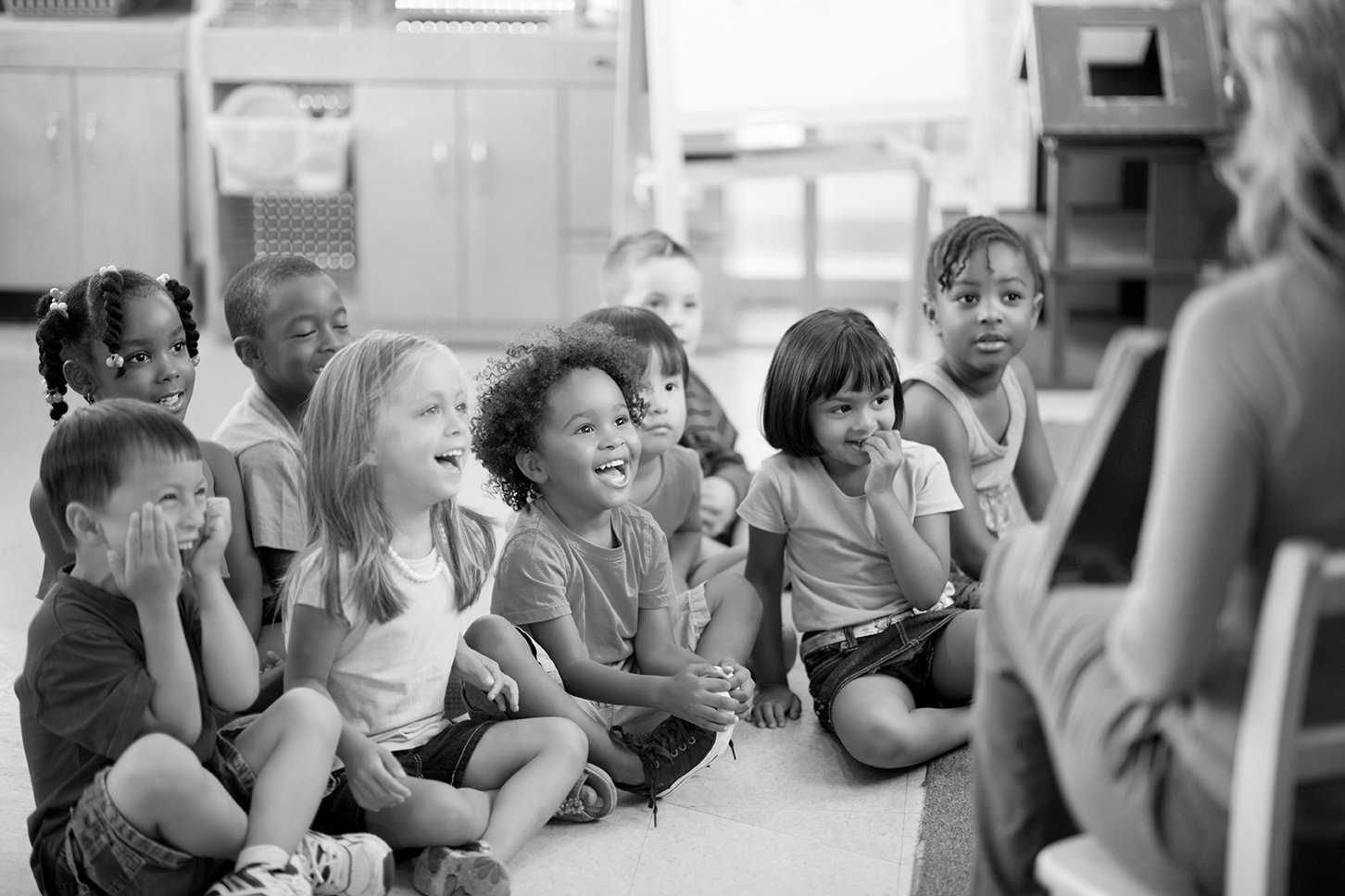 A classroom of 9 students smiling and laughing as a teacher shows the something from the front of the classroom.