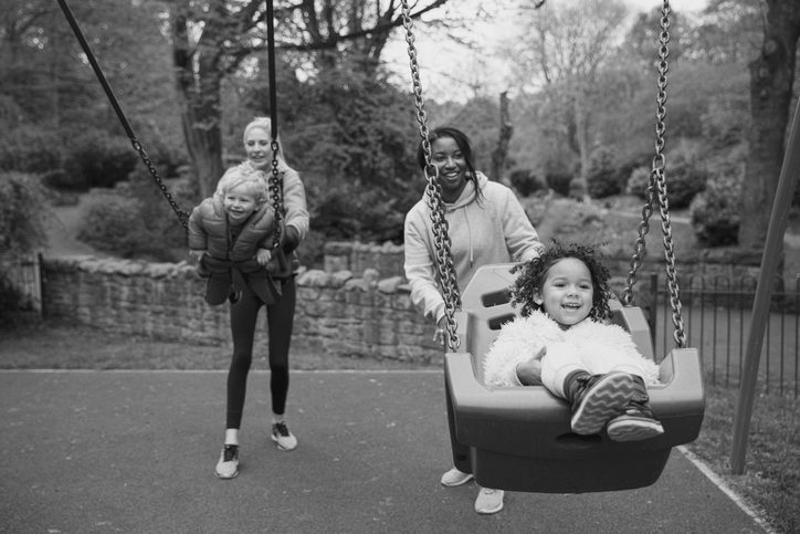 two parents and two children at the park playing on the swings.